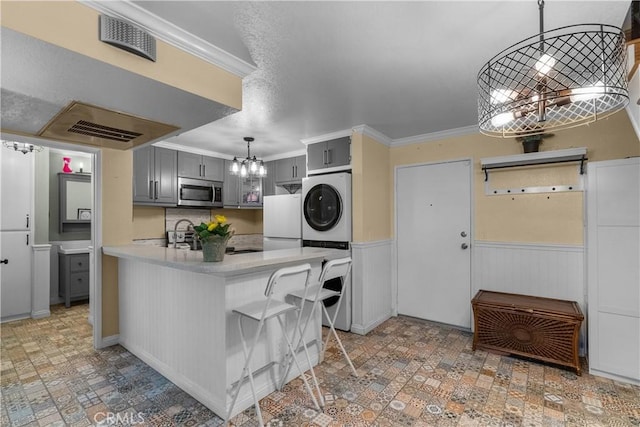 kitchen with white refrigerator, kitchen peninsula, stacked washer and dryer, a kitchen bar, and gray cabinets