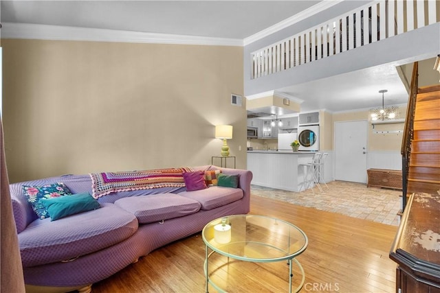 living room with a towering ceiling, light hardwood / wood-style floors, crown molding, and a notable chandelier