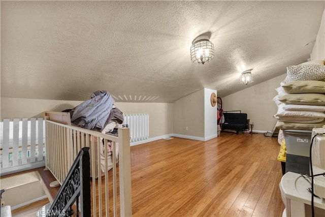 additional living space with a textured ceiling, radiator heating unit, vaulted ceiling, and hardwood / wood-style flooring