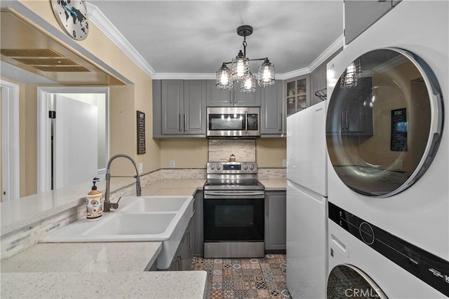 kitchen with light stone counters, gray cabinetry, stainless steel appliances, sink, and stacked washer and dryer