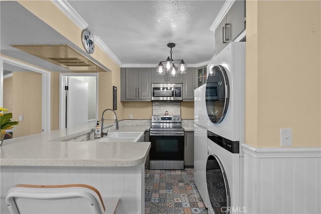 kitchen with gray cabinetry, kitchen peninsula, stacked washing maching and dryer, and appliances with stainless steel finishes