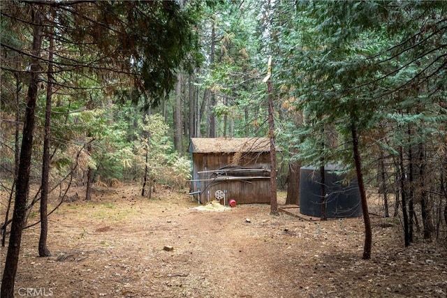 view of yard featuring a storage shed, an outdoor structure, and a view of trees