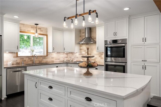 kitchen featuring white cabinetry, sink, wall chimney exhaust hood, pendant lighting, and appliances with stainless steel finishes