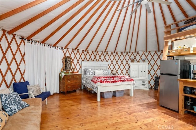 bedroom with freestanding refrigerator, lofted ceiling with beams, and light wood finished floors