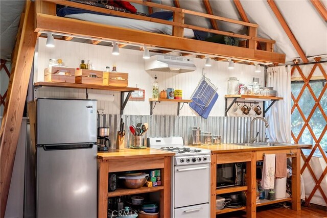 kitchen with exhaust hood, sink, white gas range oven, black microwave, and stainless steel refrigerator