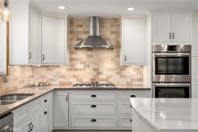 kitchen with white cabinetry, wall chimney range hood, sink, and appliances with stainless steel finishes