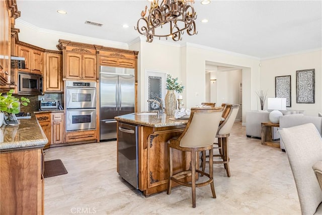 kitchen featuring backsplash, an inviting chandelier, crown molding, built in appliances, and an island with sink