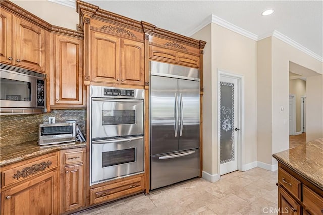 kitchen with built in appliances, crown molding, and dark stone counters