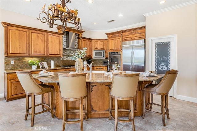 kitchen featuring built in appliances, crown molding, light stone countertops, and a kitchen island with sink