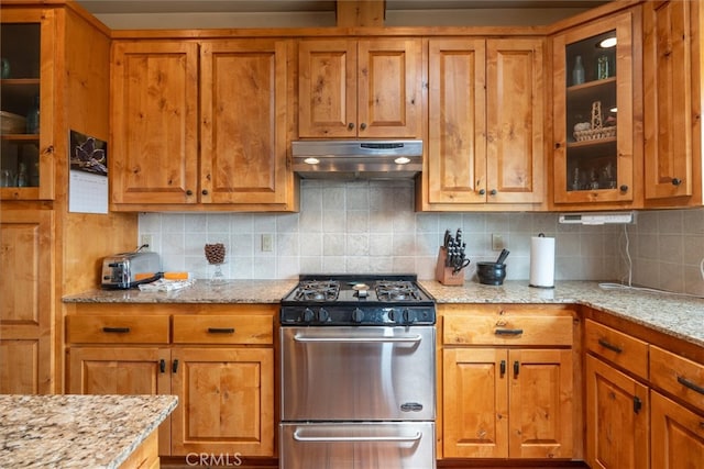 kitchen with stainless steel gas stove, light stone counters, and tasteful backsplash