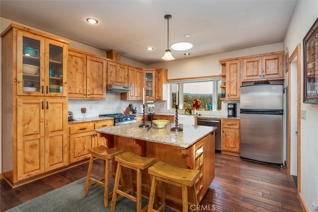 kitchen featuring appliances with stainless steel finishes, hanging light fixtures, a kitchen island, and dark hardwood / wood-style floors