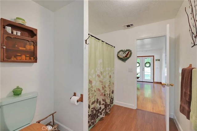 bathroom with wood-type flooring, toilet, a shower with shower curtain, and french doors