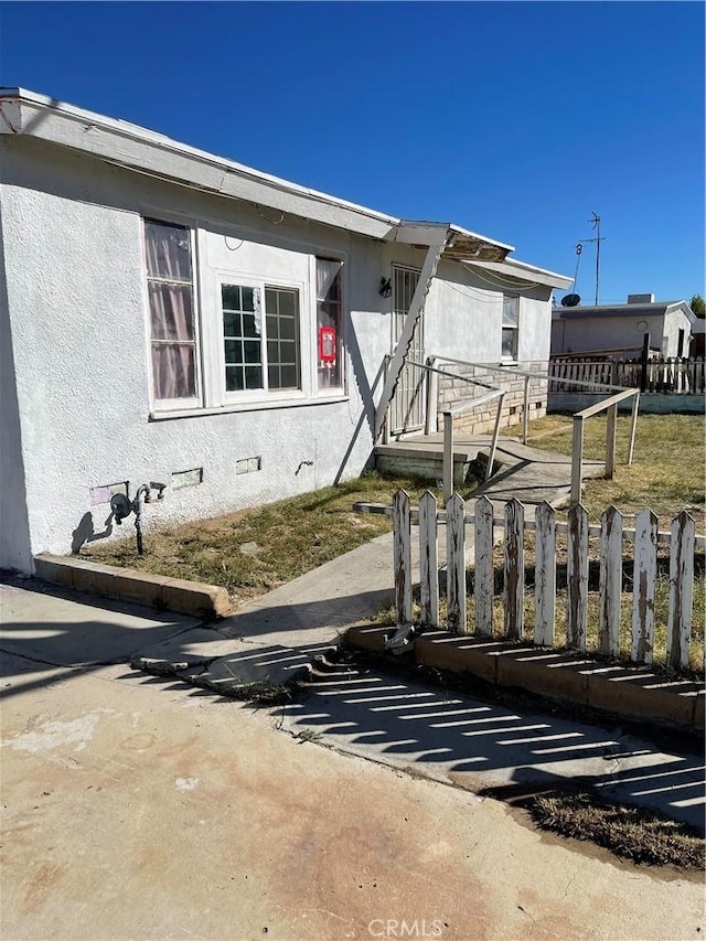 view of front facade featuring stucco siding, crawl space, and fence