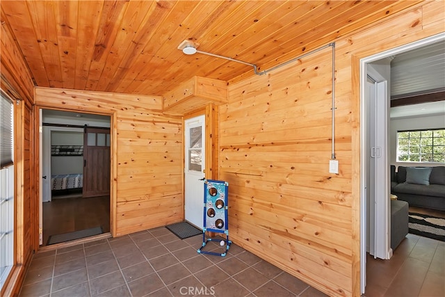 workout room with a barn door, wooden ceiling, wooden walls, and dark tile patterned floors