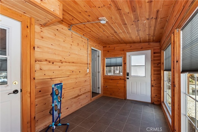 entryway with wooden ceiling, dark tile patterned flooring, a wealth of natural light, and wooden walls