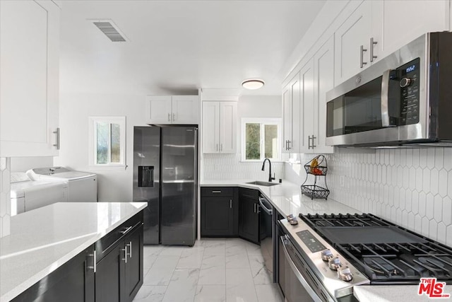 kitchen featuring independent washer and dryer, white cabinets, backsplash, stainless steel appliances, and sink