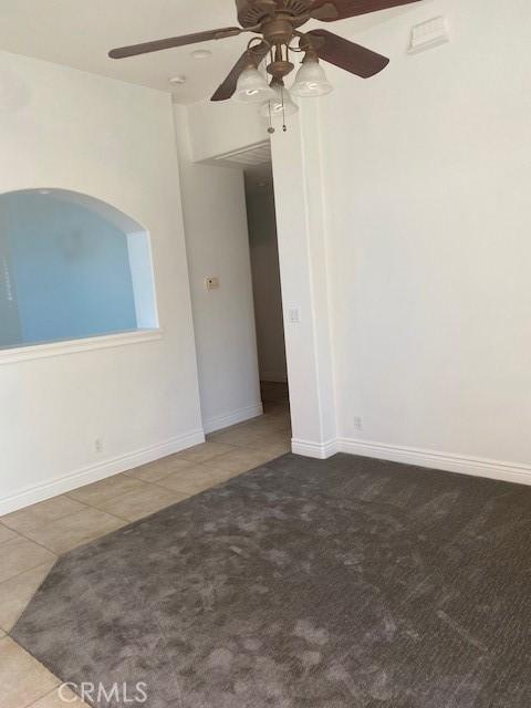 tiled empty room with baseboards, carpet, and a ceiling fan