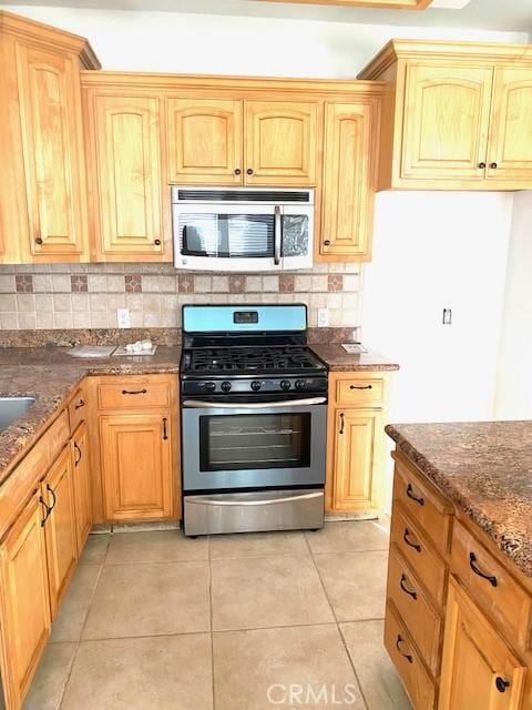 kitchen featuring backsplash, light tile patterned floors, appliances with stainless steel finishes, and dark stone countertops