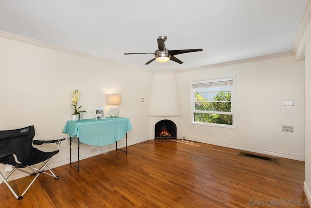 unfurnished room with wood-type flooring, crown molding, ceiling fan, and a large fireplace