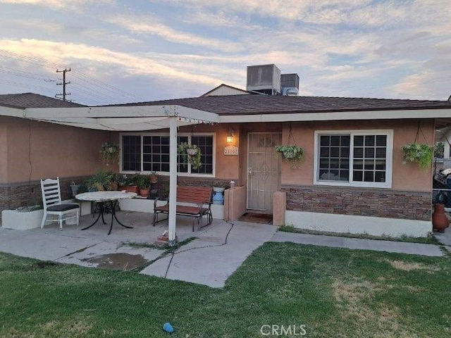 exterior entry at dusk with central air condition unit, a patio area, and a yard