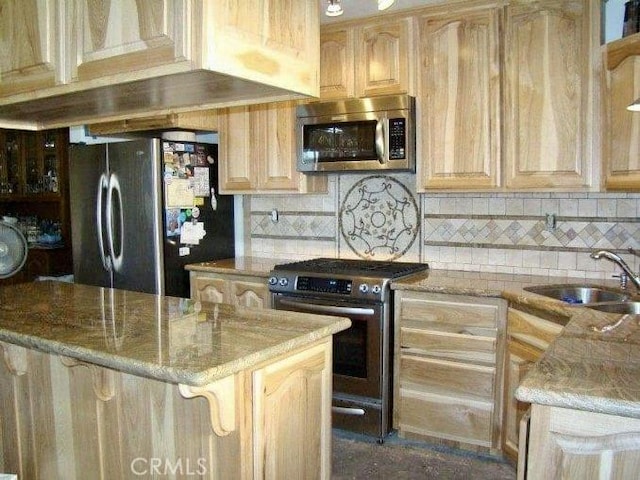 kitchen featuring a center island, light stone countertops, light brown cabinets, and appliances with stainless steel finishes