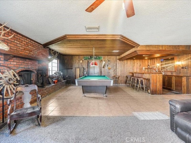 rec room featuring wooden walls, a brick fireplace, tile patterned flooring, a textured ceiling, and pool table