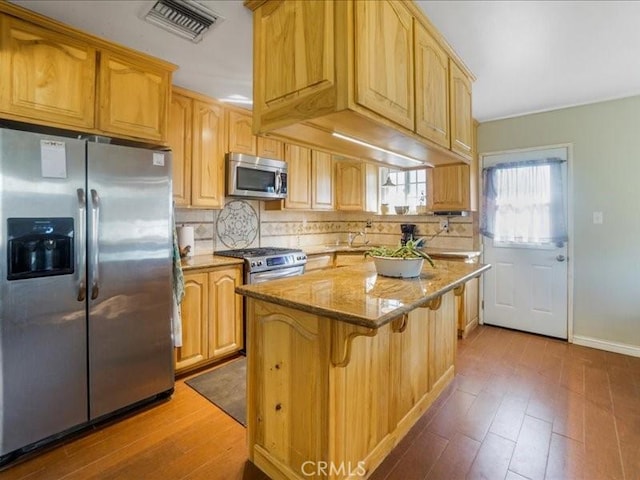 kitchen with a center island, dark hardwood / wood-style flooring, light stone countertops, and appliances with stainless steel finishes