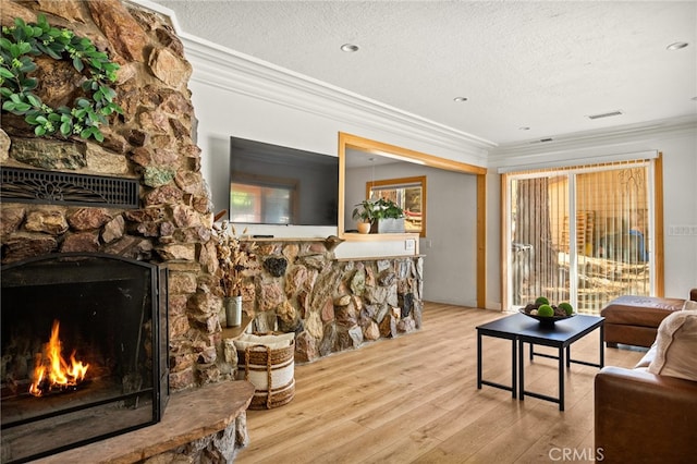 living room featuring a stone fireplace, ornamental molding, a textured ceiling, and light wood-type flooring