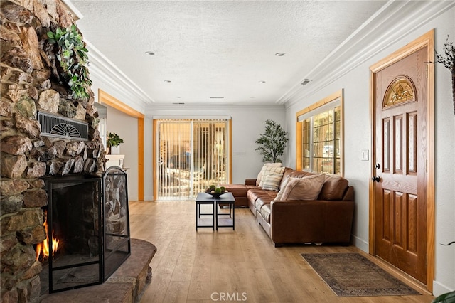 living room featuring a stone fireplace, crown molding, light hardwood / wood-style floors, and a wealth of natural light