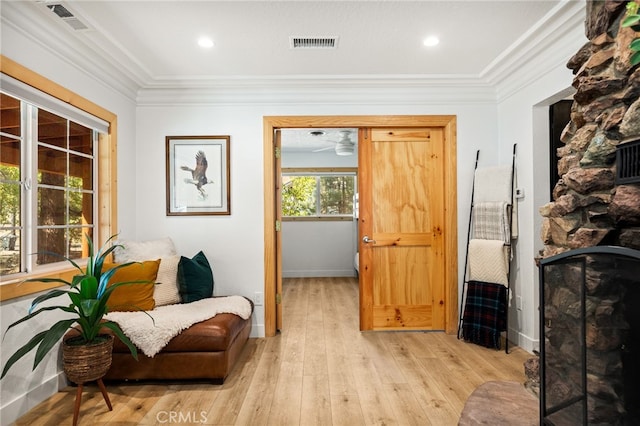 living area with a stone fireplace, light hardwood / wood-style flooring, ceiling fan, and crown molding