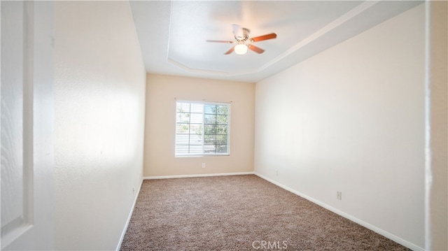 carpeted spare room featuring a raised ceiling and ceiling fan