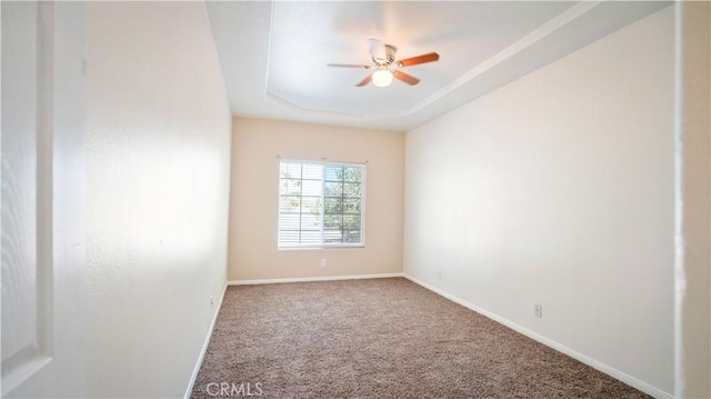 unfurnished room with a tray ceiling, carpet, a ceiling fan, and baseboards