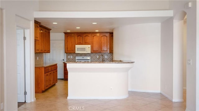 kitchen with white microwave, decorative backsplash, brown cabinetry, range, and light tile patterned floors