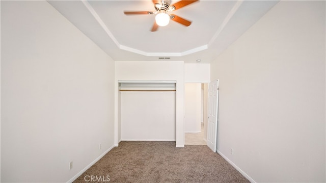 unfurnished bedroom featuring light colored carpet, a closet, a tray ceiling, and ceiling fan