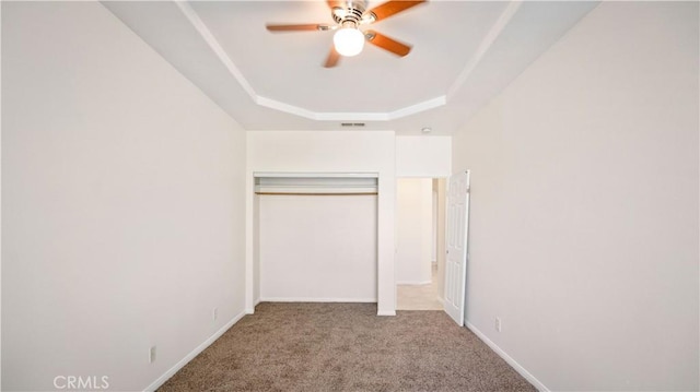 unfurnished bedroom featuring a tray ceiling, a ceiling fan, carpet floors, a closet, and baseboards