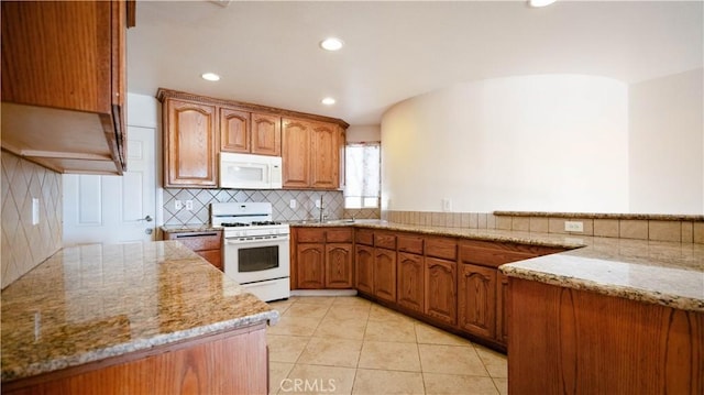 kitchen featuring recessed lighting, backsplash, white appliances, brown cabinets, and light stone counters