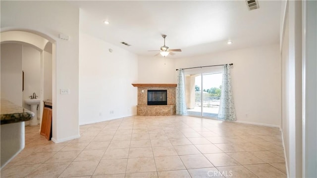 unfurnished living room with a ceiling fan, visible vents, a fireplace, and light tile patterned floors