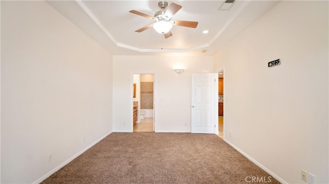 unfurnished bedroom with light carpet, a tray ceiling, visible vents, baseboards, and ensuite bath