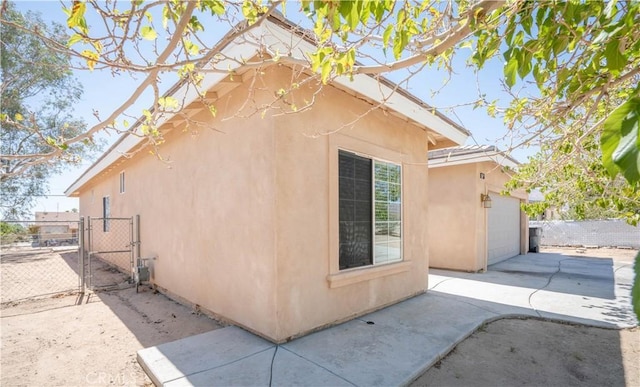 view of side of home featuring a gate, fence, stucco siding, an attached garage, and driveway