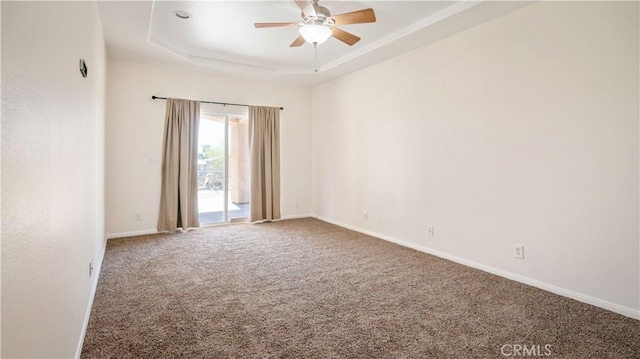 spare room featuring a raised ceiling, carpet, a ceiling fan, and baseboards