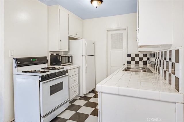 kitchen with tile counters, tasteful backsplash, sink, white cabinetry, and white appliances