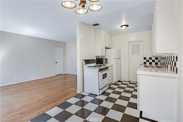 kitchen with white cabinets, white appliances, backsplash, dark wood-type flooring, and tile countertops