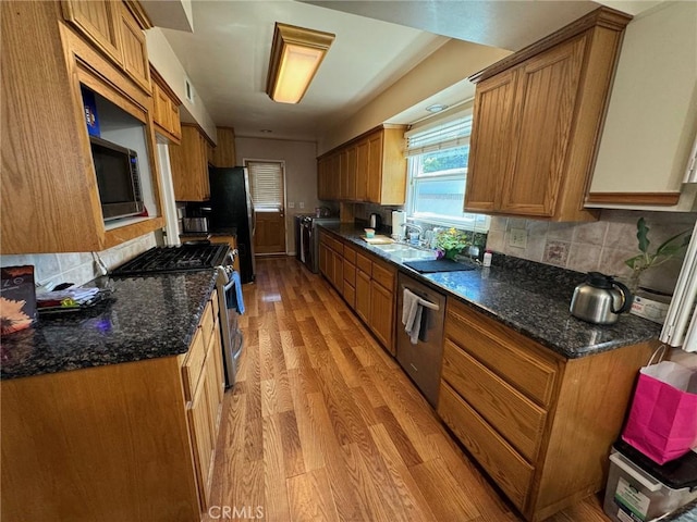 kitchen with independent washer and dryer, light hardwood / wood-style floors, stainless steel appliances, sink, and backsplash