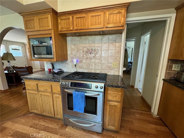 kitchen featuring light hardwood / wood-style floors, stainless steel appliances, dark stone countertops, and tasteful backsplash