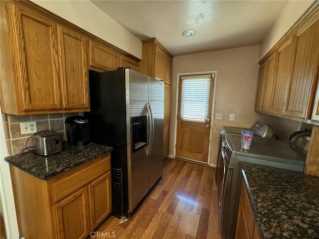 kitchen with independent washer and dryer, backsplash, dark stone counters, dark hardwood / wood-style floors, and stainless steel fridge with ice dispenser