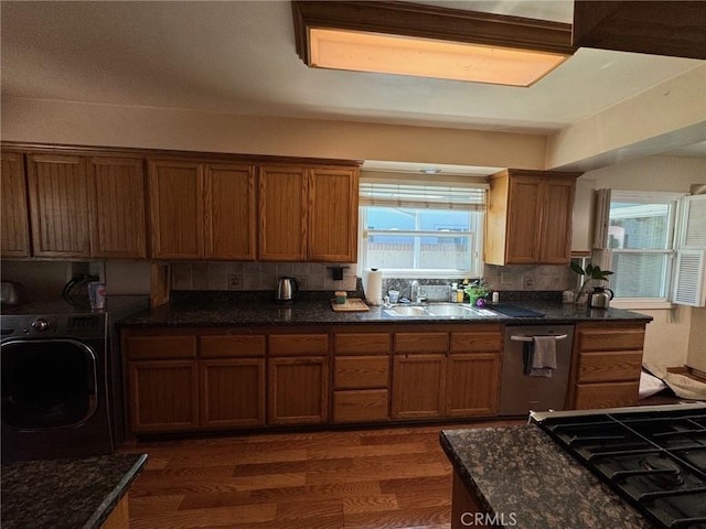 kitchen with sink, stainless steel dishwasher, a healthy amount of sunlight, washer / dryer, and dark hardwood / wood-style flooring