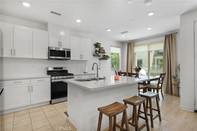 kitchen featuring visible vents, a breakfast bar, stainless steel appliances, white cabinetry, and a sink