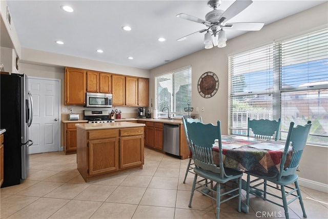 kitchen with stainless steel appliances, ceiling fan, sink, light tile patterned floors, and a kitchen island