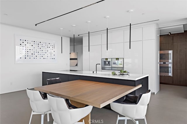 kitchen with a kitchen breakfast bar, white cabinets, wood walls, electric stovetop, and a center island with sink