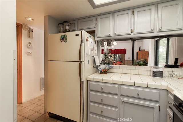 kitchen with gray cabinets, white refrigerator, tile counters, tasteful backsplash, and light tile patterned floors